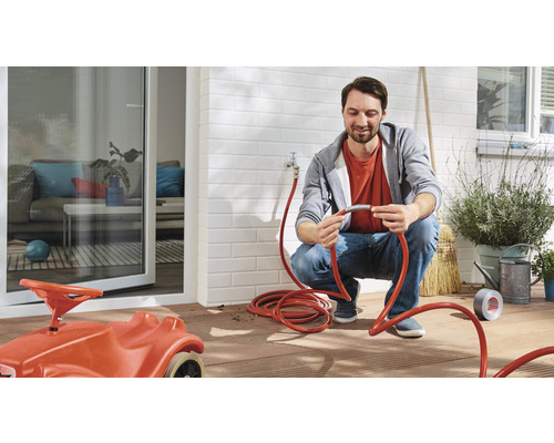 Un homme connecte un tuyau d''arrosage à un robinet extérieur.