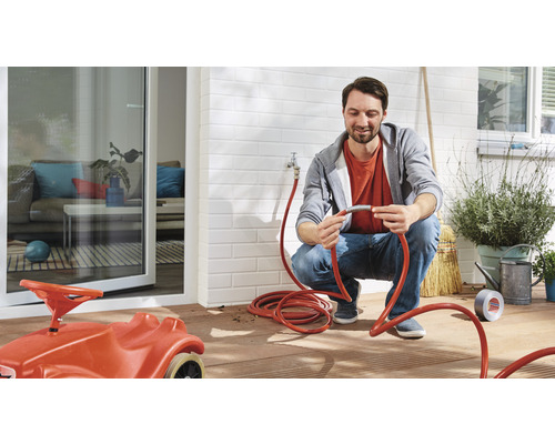 Mann verbindet einen Gartenschlauch im Aussenbereich, mit Kinderspielzeugauto im Vordergrund