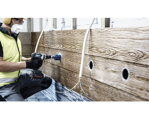 Un artisan perce un trou dans un mur en bois avec une perceuse pour les installations électriques.