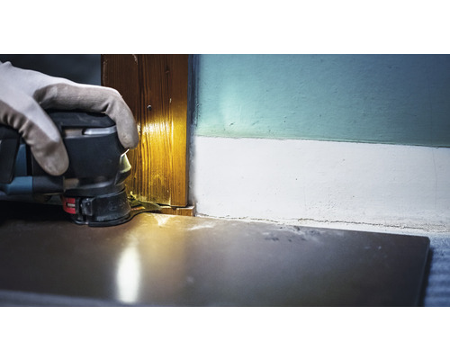 Eine Person verwendet einen Multifunktionsschleifer zum Schleifen einer Holztürleiste.