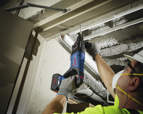 Un homme perce un plafond en béton avec un perforateur.