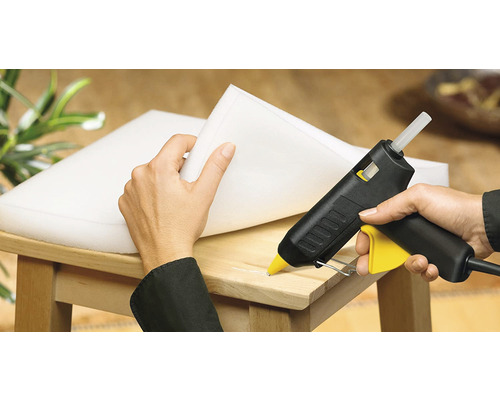 Une personne fixe de la mousse sur une chaise en bois avec un pistolet à colle chaude.