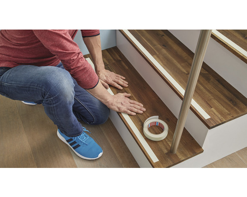 Un homme fixe une bande antidérapante sur un escalier en bois.