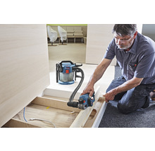 Artisan travaillant avec un rabot électrique et un aspirateur dans une pièce.