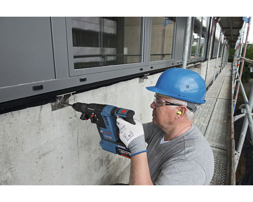 Un homme perce un trou dans un mur sur un échafaudage à l'aide d'un perforateur