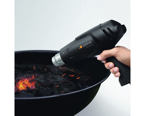 Une main tient un pistolet à air chaud Steinel HL 1821 S au-dessus d''un barbecue à charbon.