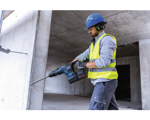 Ein Bauarbeiter bohrt mit einem Bohrhammer ein Loch in eine Betonwand.