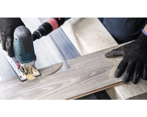 Une scie sauteuse coupe une planche de stratifié. Des gants de protection sont portés.