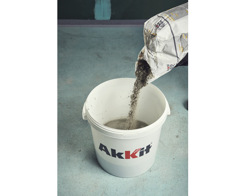 Une personne verse du béton sec d''un sac dans un seau.