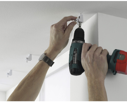 Une personne fixe une tringle à rideaux au plafond à l''aide d''une visseuse sans fil.