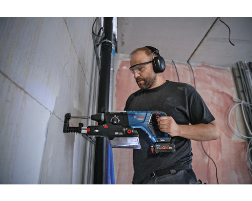 Artisan avec lunettes de protection et protection auditive perçant un trou dans un mur avec un marteau perforateur.