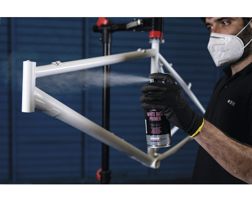 Une personne applique un apprêt blanc sur un cadre de vélo à l''aide d''un aérosol.