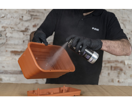 Eine Person sprüht eine Pflanzschale mit Sprühfarbe.