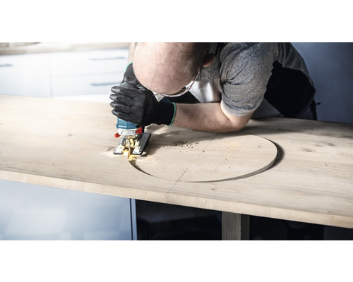 Mann sägt mit einer Stichsäge ein Loch in eine Holzplatte.