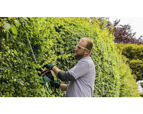Un homme taille une haie avec un taille-haie dans le jardin.