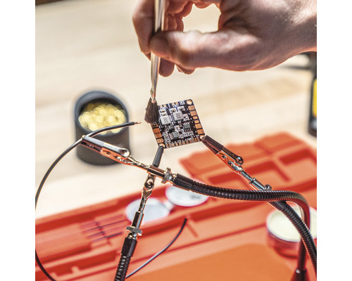 Nettoyage d''une carte de circuit imprimé avec un pinceau, fixée par des pinces crocodiles.