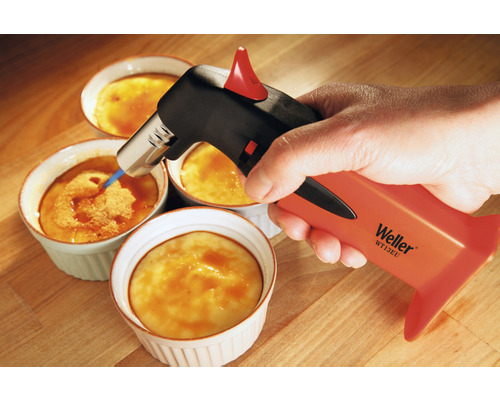 Une main caramélise une crème brûlée avec un brûleur.