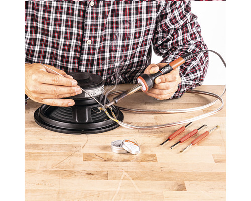 Un homme soude un haut-parleur avec un fer à souder, de l''étain et des outils sur une table en bois