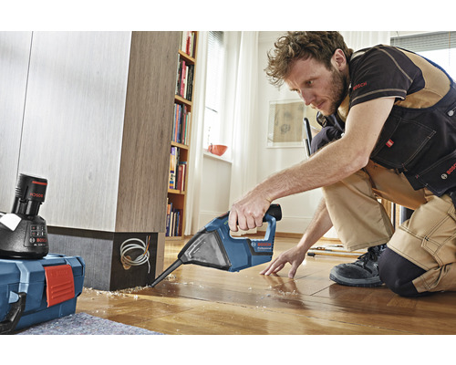 Un homme travaille avec un perforateur sur un plancher en bois dans une pièce.