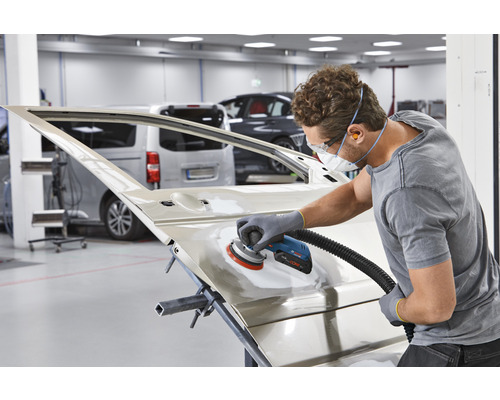 Un homme ponce une portière de voiture avec une ponceuse dans un atelier.