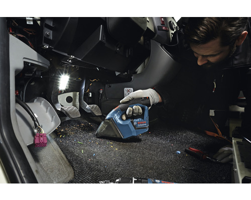 Ein Mann saugt mit einem Akkusauger den Fussraum eines Fahrzeugs.