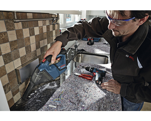 Ein Mann saugt mit einem Akku-Handsauger Späne von einer Küchenarbeitsplatte. Werkzeuge liegen bereit.