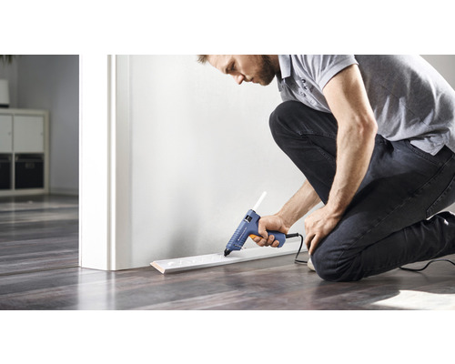 Homme fixant une plinthe avec un pistolet à colle chaude