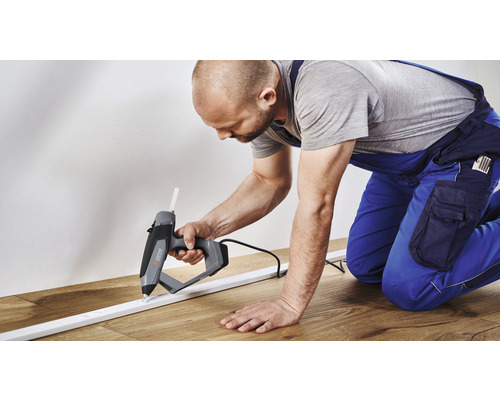 Handwerker verwendet Heißklebepistole zum Anbringen einer Fußleiste.