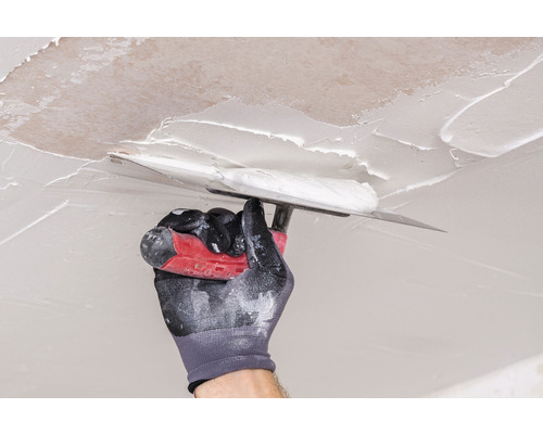 Hand mit Handschuh glättet Spachtelmasse an einer Decke