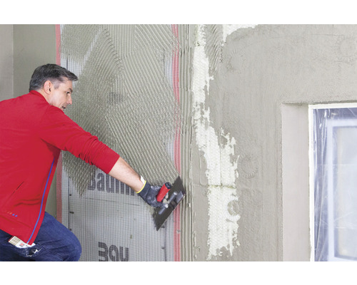 Un homme applique de la colle sur un panneau d''isolation thermique sur un chantier.