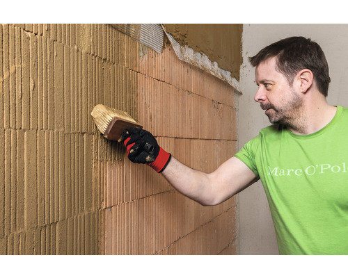 Ein Mann trägt Putz auf eine Ziegelwand auf