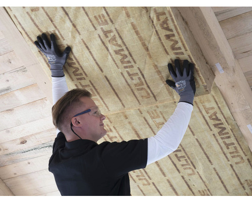 Un homme fixe de la laine isolante à un plafond en bois.