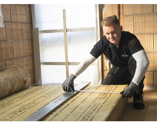 Un artisan mesure de la laine d''isolation avec un instrument de mesure sur un chantier de construction.