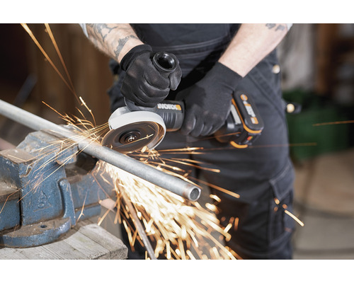 Une personne utilise une meuleuse d''angle pour couper un tube métallique fixé dans un étau, ce qui provoque des étincelles.