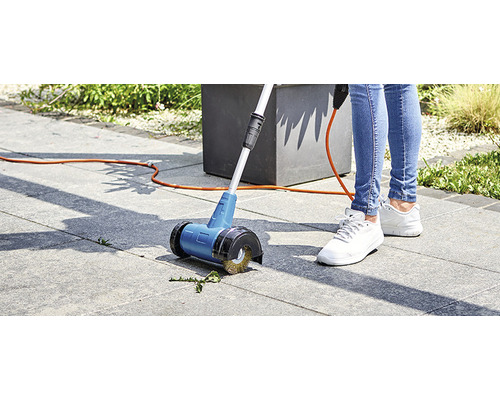Person benutzt einen Fugenkratzer mit Elektroanschluss auf Pflastersteinen im Garten.