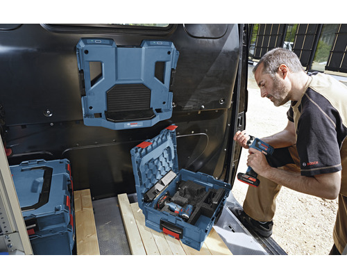 Un artisan dans l''espace de chargement d''un transporteur avec une boîte à outils, un système d''étagères monté et un outil sans fil à la main.