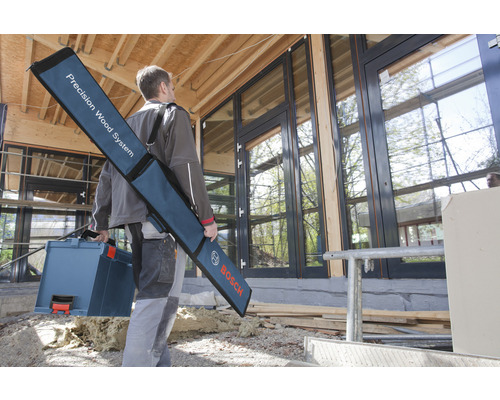 Un homme porte une caisse à outils et un sac avec un système de travail du bois de précision devant une maison avec des fenêtres