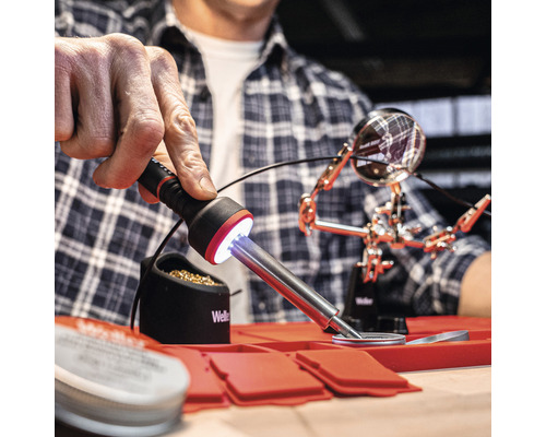 Personne utilisant un fer à souder sur un tapis résistant à la chaleur avec une station de soudage et une troisième main