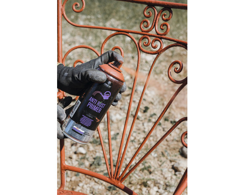 Eine Person sprüht mit einer Rostschutzgrundierung ein Metallgeländer ein.