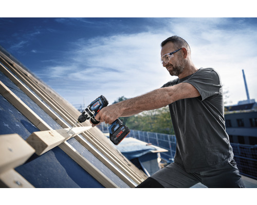 Un homme travaille avec une visseuse sans fil sur un toit.