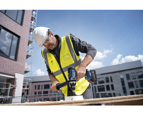 Un ouvrier perce un trou dans une planche de bois avec une perceuse sans fil.