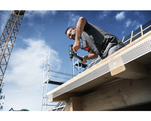 Un artisan fixe un profilé de rive sur un toit à l'aide d'une visseuse sans fil.