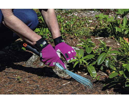 Une personne ratisse des déchets de jardin avec un râteau, protégé par des gants de jardinage.
