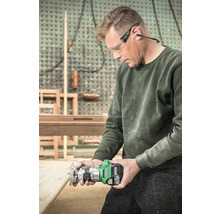 Ein Mann benutzt eine Oberfräse mit Akku für Holzarbeiten, während er eine Schutzbrille und Ohrenschützer trägt.