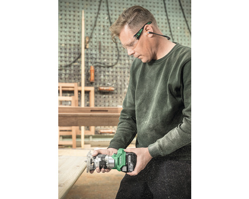 Ein Mann benutzt eine Oberfräse mit Akku für Holzarbeiten, während er eine Schutzbrille und Ohrenschützer trägt.