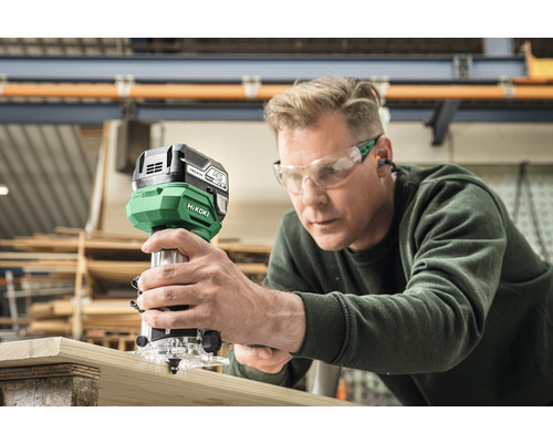 Ein Mann benutzt eine Hikoki Oberfräse an einem Holzbrett in einer Werkstatt.