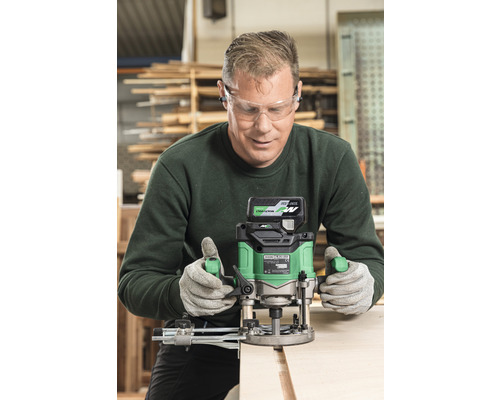 Handwerker mit Schutzbrille und Gehörschutz beim Arbeiten mit einer Oberfräse an einem Holzstück.