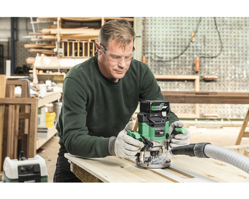 Un homme utilise une défonceuse sur une planche de bois dans un atelier.
