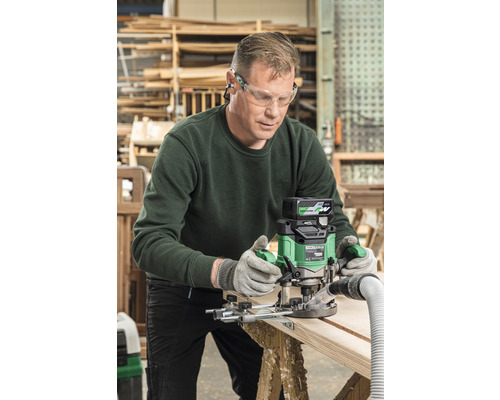 Un homme travaille une planche de bois avec une défonceuse dans un atelier.