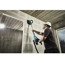 Un homme lisse un mur avec une ponceuse à long manche dans un chantier de construction.